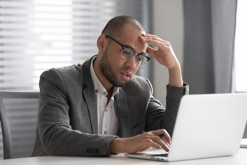 Man frustrated and upset looking at laptop with hand on forehead