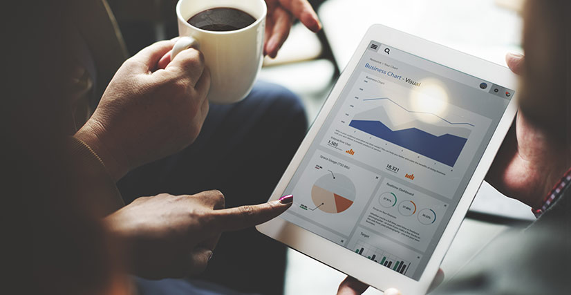 Close up of staff members gathered around a tablet looking at business analytics