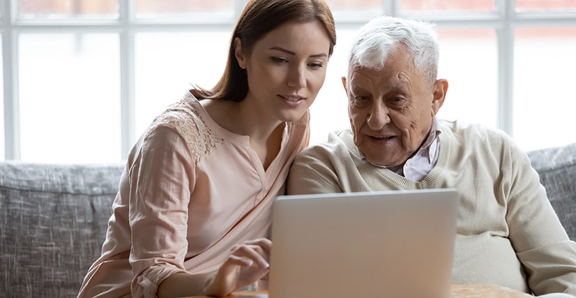Woman sitting with senior father on couch on laptop